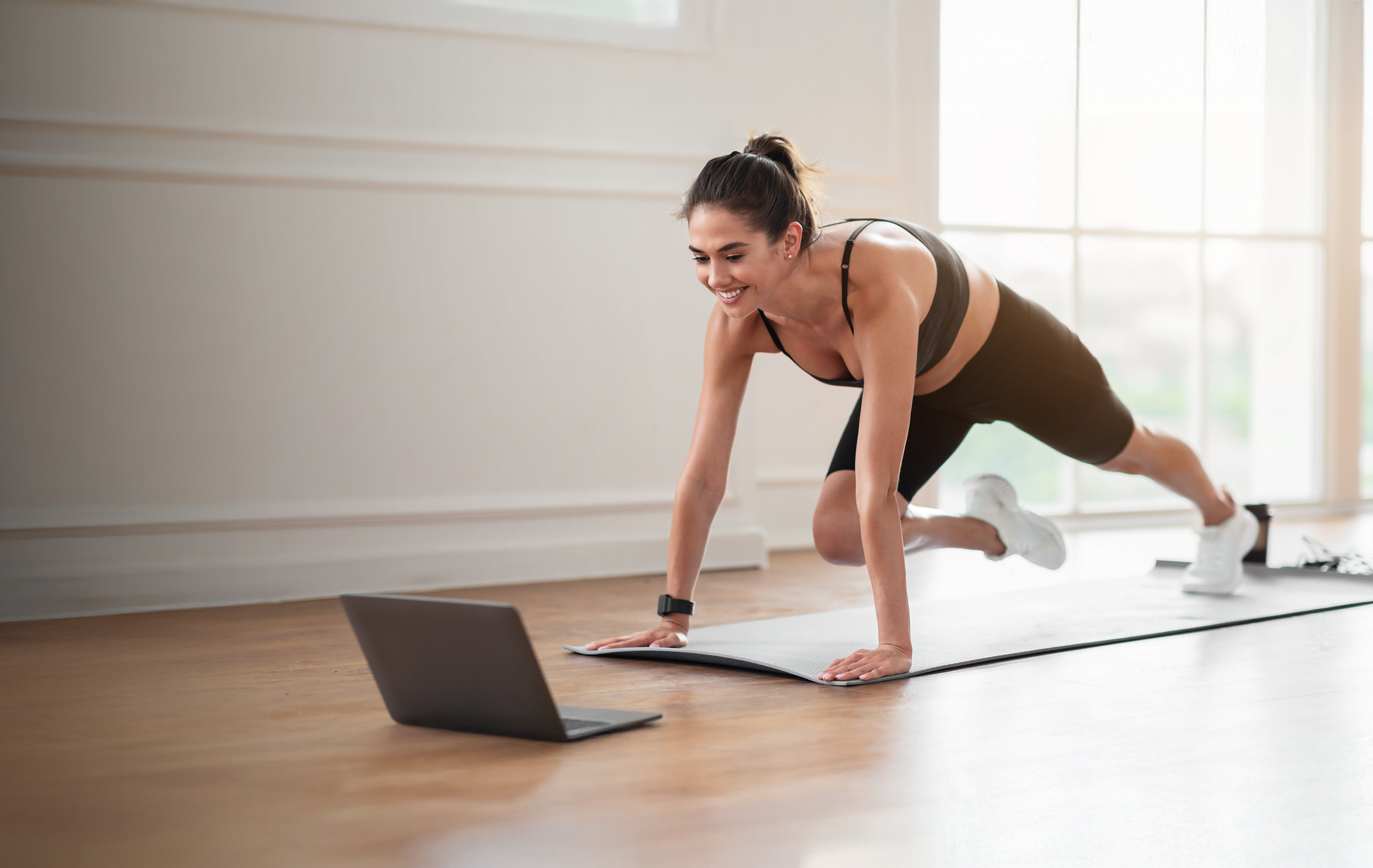 Donna che si allena a casa seguendo un programma di fitness online sul laptop